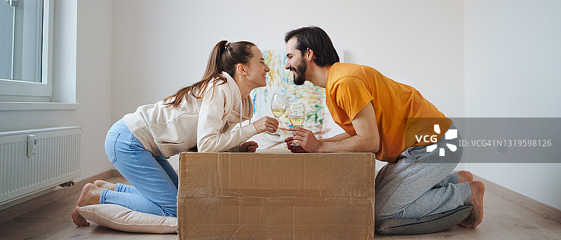 年轻夫妇带着盒子和葡萄酒搬进新公寓，新家和搬迁概念。图片素材