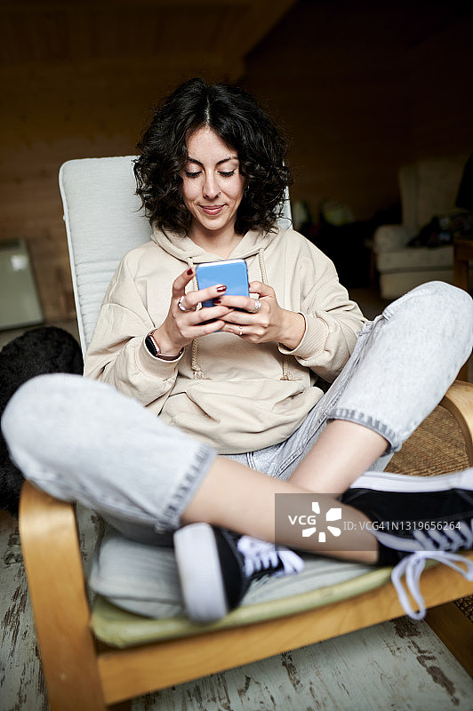 微笑的女人盘腿坐在家里用手机图片素材
