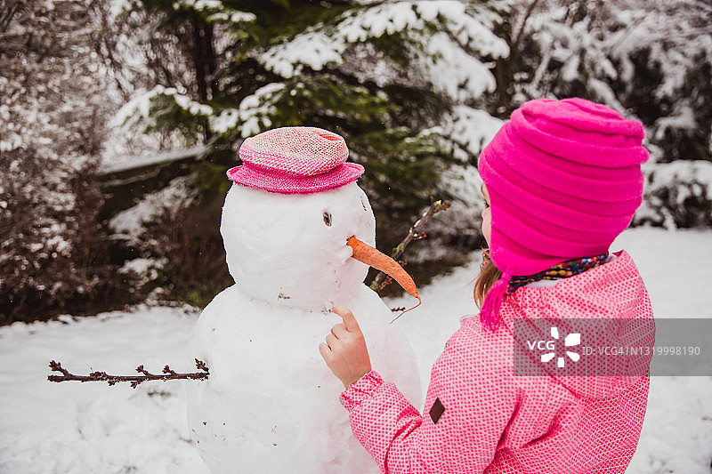 冬天，穿着冬衣的女孩在自家后院堆雪人图片素材