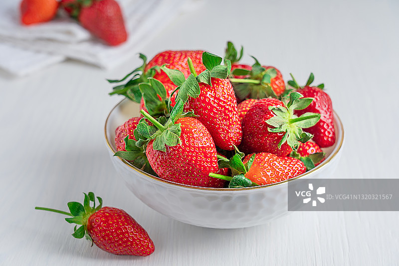 白木桌上放一碗鲜亮的成熟红草莓图片素材