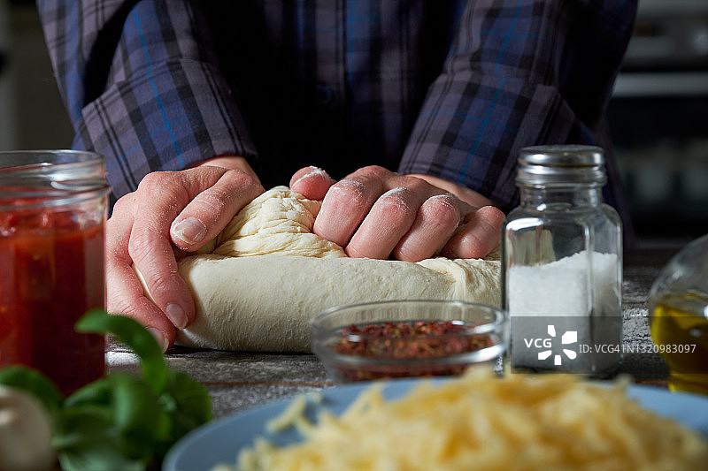 在家里的木桌上用蔬菜和蘑菇烹饪意大利素食披萨。女人用手揉面，揉面。一步一步的指导，自己做。步骤1。图片素材