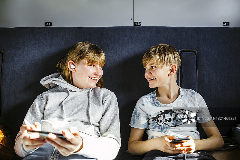 微笑的哥哥和妹妹在火车上用智能手机看着对方图片素材