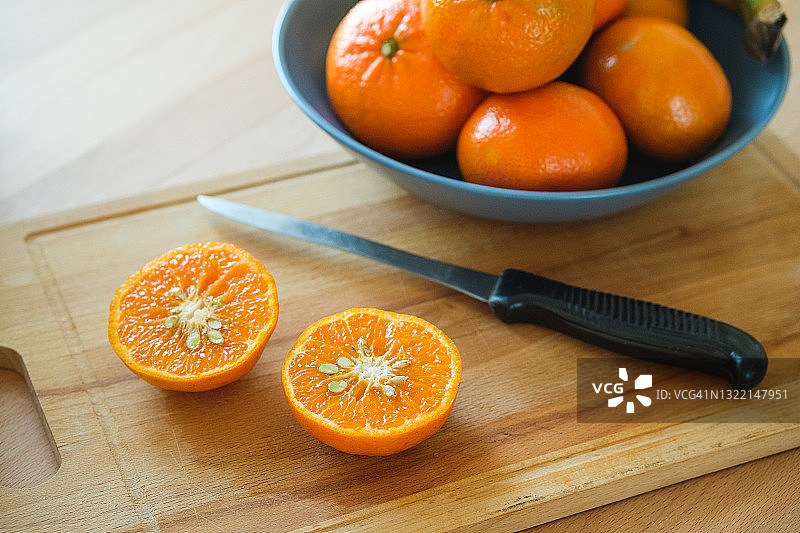 把带骨的橘子切成两半，放在砧板上。它旁边是一盘完整的水果，靠在一张木制餐桌上。素食、纯素和生食。有机农家产品的概念。图片素材