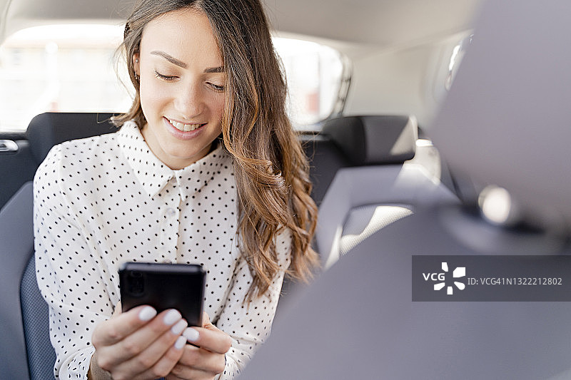 微笑的女企业家坐在车里使用智能手机图片素材