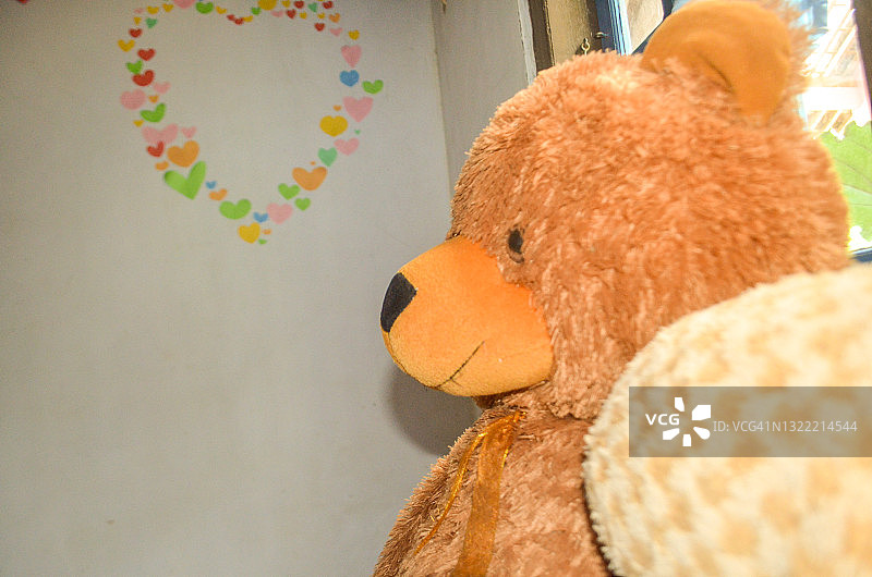 一个棕色的泰迪熊，背景是一个女孩的房间图片素材