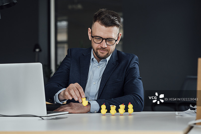 男企业家拿着笔记本电脑，拿着小鸡玩具在办公室图片素材