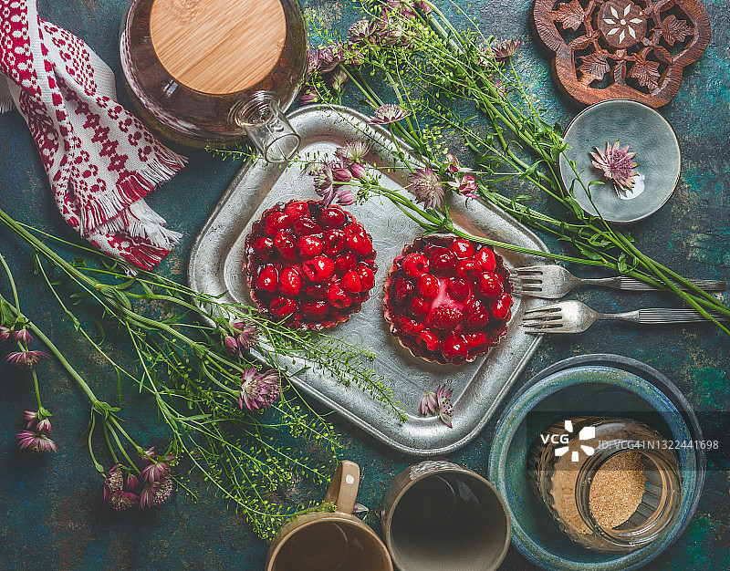 红色莓果馅饼在复古的银方形盘子上，绿色和蓝色的餐桌上有鲜花和厨房用具图片素材