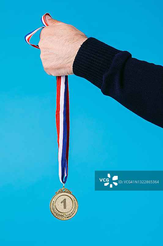 一个老年运动员的手臂持有第一名金牌的细节，在蓝色的背景。图片素材