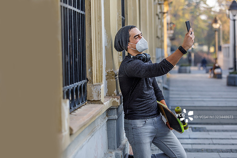 英俊的年轻人在一个城市里用着手机玩滑板。图片素材