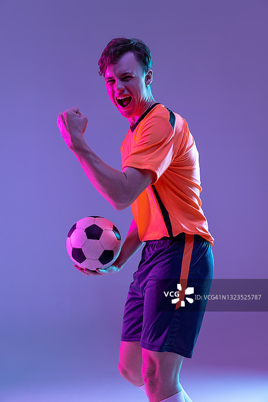 半长肖像的职业足球运动员站在孤立的梯度蓝粉色背景霓虹灯。运动的概念，美。图片素材