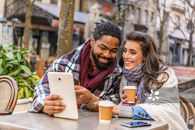 一个快乐的现代多民族夫妇正在一起放松在咖啡馆和使用平板电脑早上。图片素材