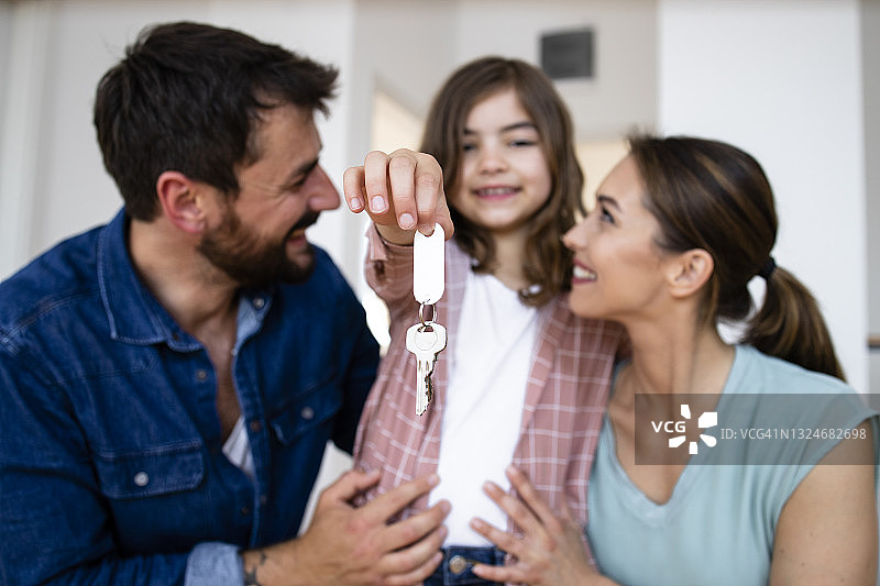 微笑的白人家庭和女儿拿着他们新家的钥匙的肖像。图片素材