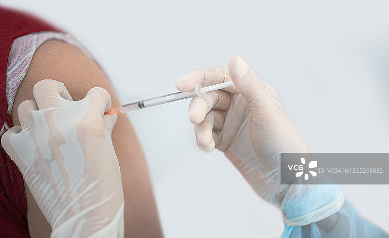 医生在病人的肩膀上接种疫苗的特写。手臂注射流感疫苗。冠状病毒Covid-19疫苗疾病准备人体临床试验接种疫苗。图片素材