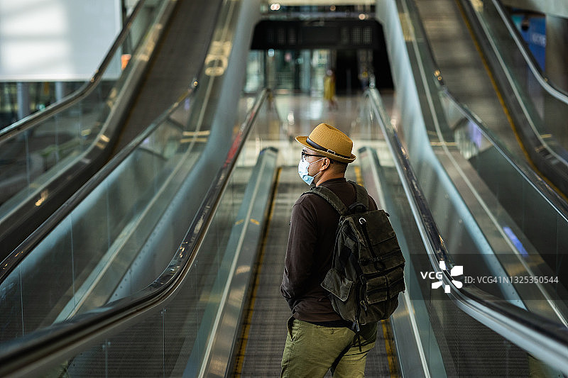 旅行者戴口罩保护流感病毒。旅客站在机场候机楼的自动扶梯上。在大流行期间必须保持社交距离自我隔离。图片素材