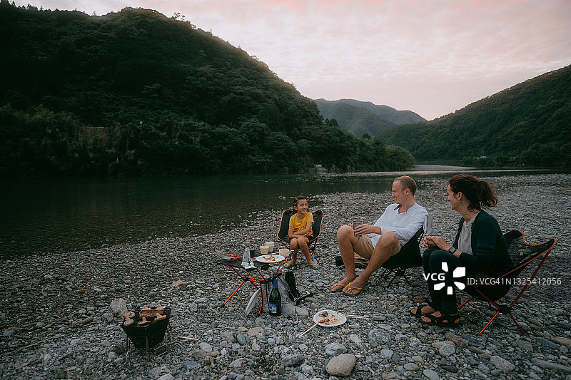 一家人在河边露营享受烧烤晚餐图片素材