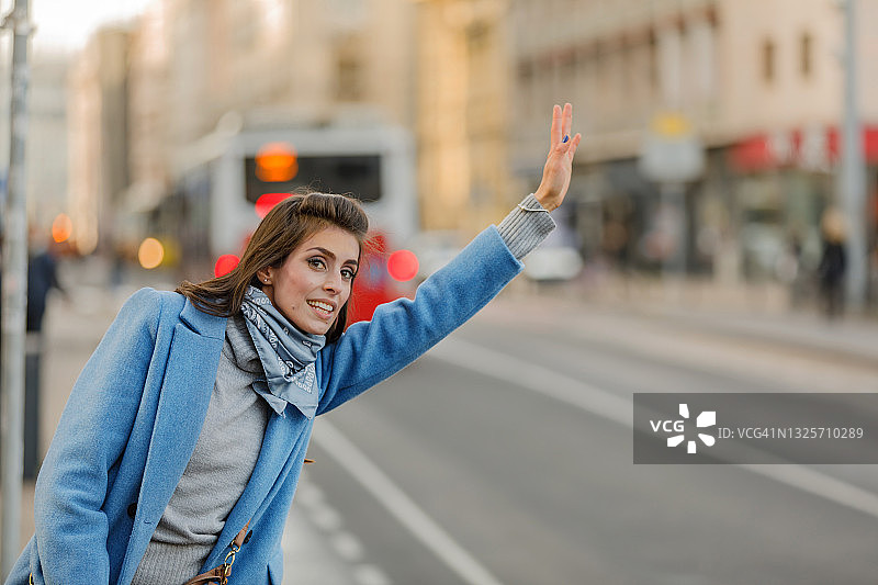 一位年轻女子站在街上挥动手臂想要搭出租车。图片素材