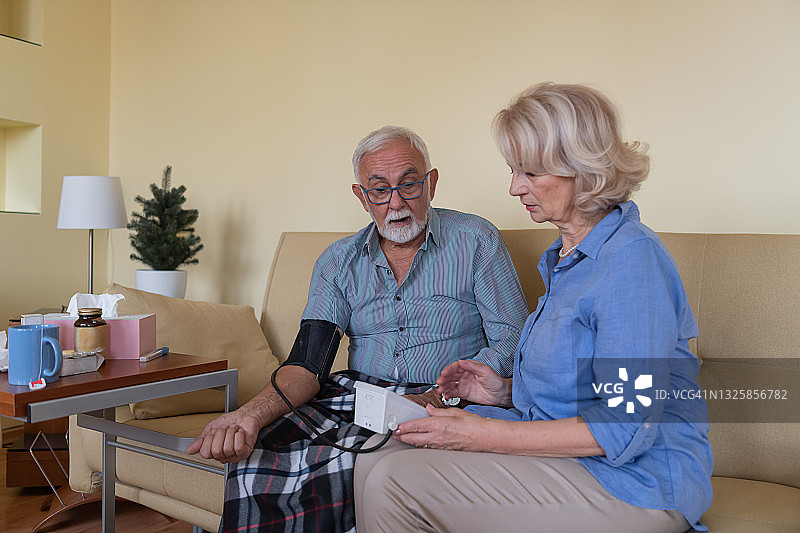 一位老年妇女用血压计为丈夫测量血压。图片素材