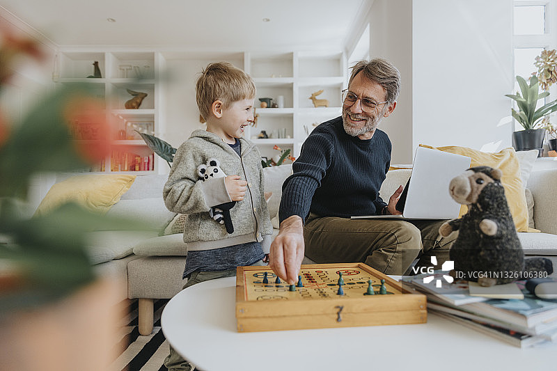 快乐的父亲和儿子在家里玩ludo游戏图片素材