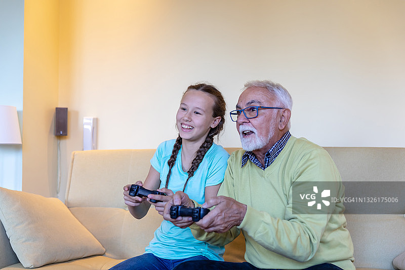 高兴的爷爷和孙女在家里用操纵杆玩电子游戏。图片素材