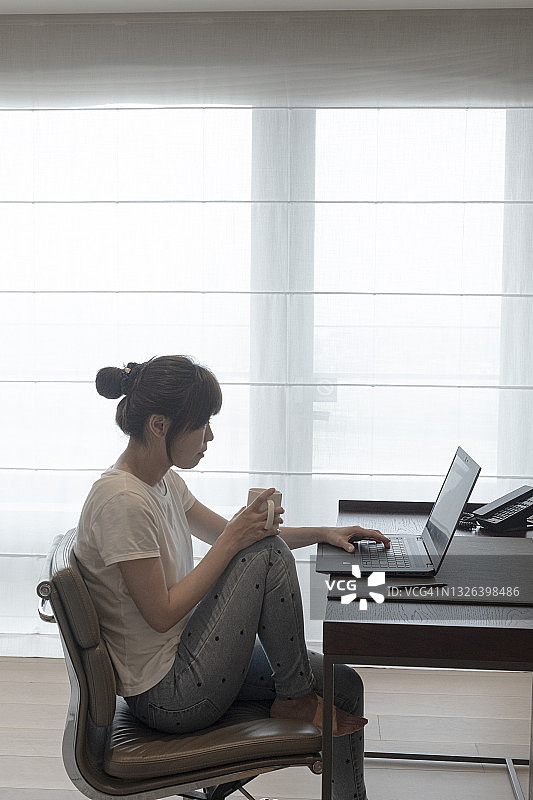 快乐的亚洲女人在家里用笔记本电脑工作图片素材
