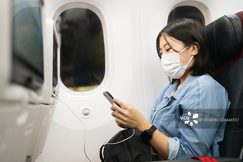 女游客戴着保护面罩坐在飞机上并使用智能手机图片素材