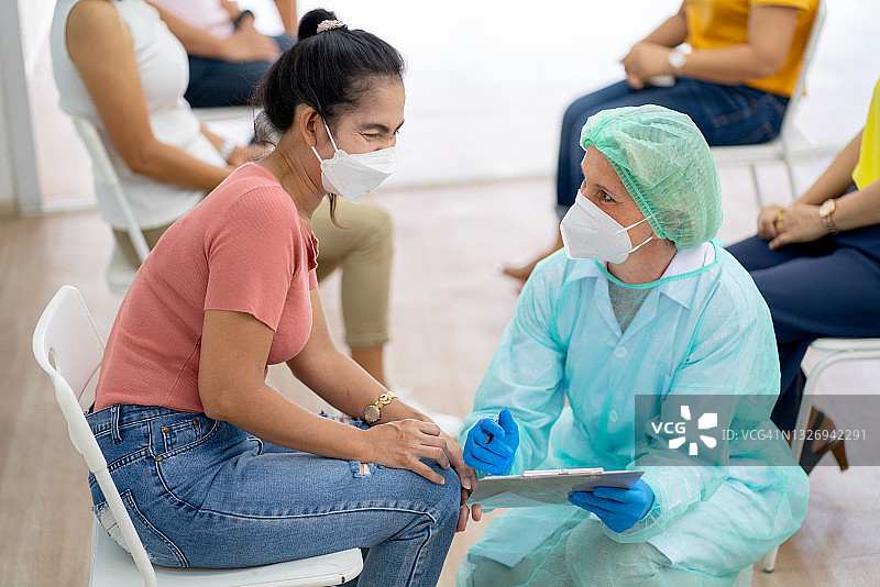 医务人员或护士与一名等待接种Covid-19疫苗的妇女坐在一起讨论图片素材