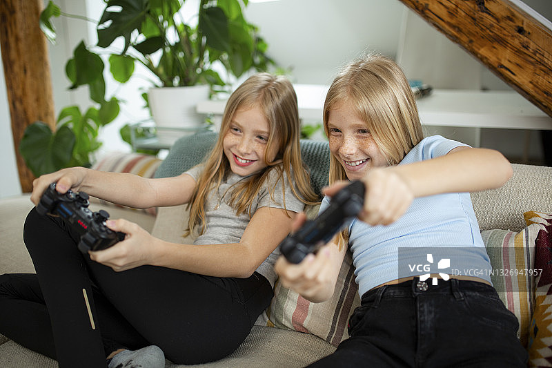 快乐的白种双胞胎姐妹在家里玩电子游戏图片素材