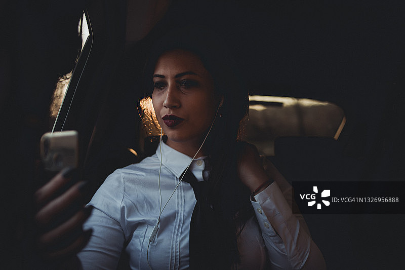 一位年轻的黑发商务女性坐在汽车后座上，去参加一个商务会议并使用手机。图片素材