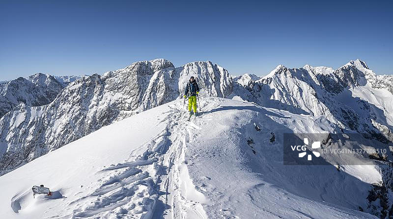 德国巴伐利亚州Garmisch-Partenkirchen的阿尔卑斯峰，前往伯纳德因科普夫阿尔卑斯峰滑雪的游客，在冬季俯瞰冰雪覆盖的Wetterstein山脉图片素材