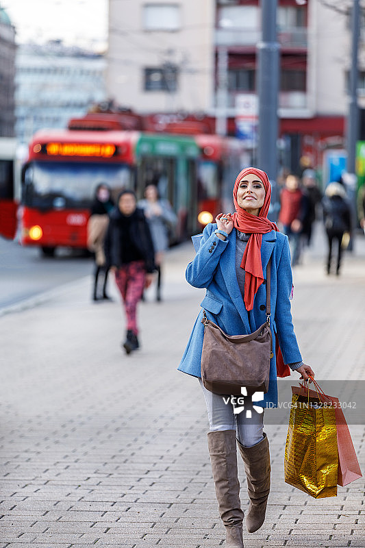 一位快乐的穆斯林妇女拿着购物袋走在街上。图片素材