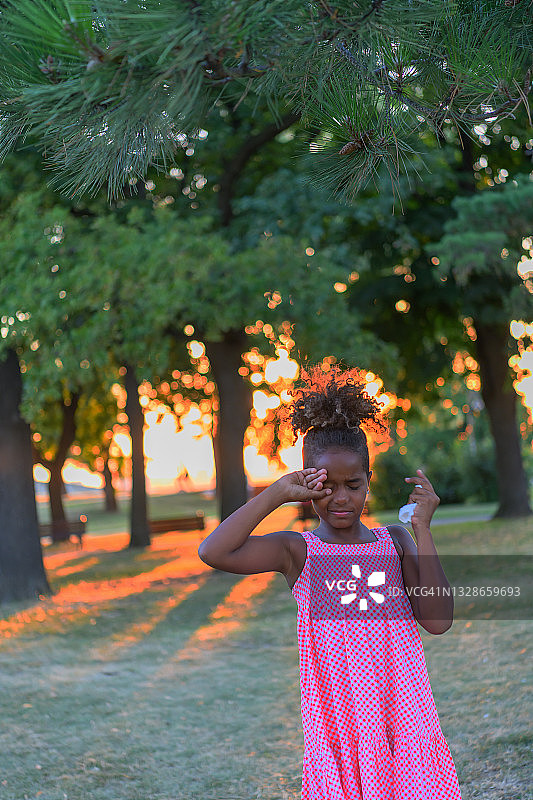 可爱的小女孩在公园揉眼睛。图片素材