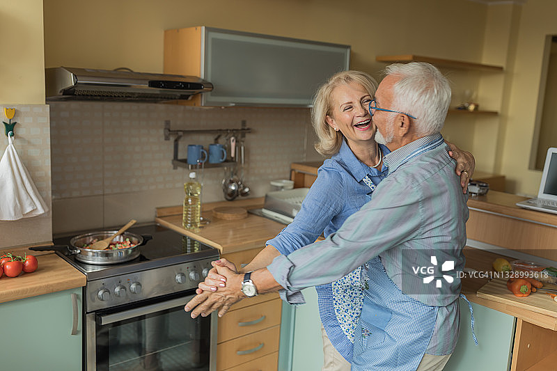 一对老年夫妇在家做饭时享受舞蹈。图片素材