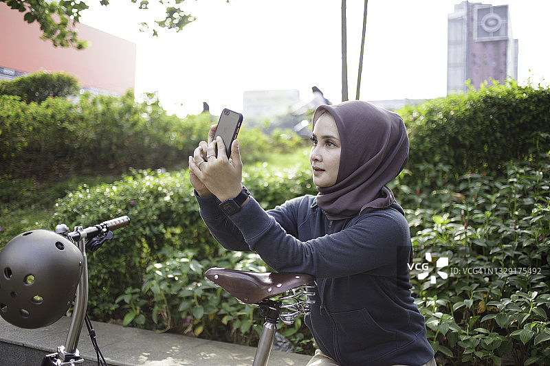一名戴头巾的亚洲年轻女子，骑完自行车后，用智能手机图片素材
