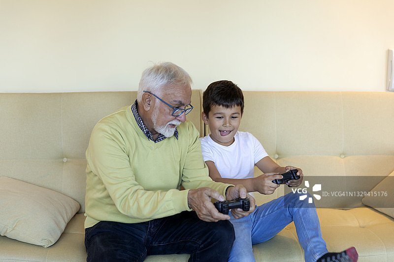 一个快乐的孩子和他的爷爷在客厅里玩电脑游戏。图片素材
