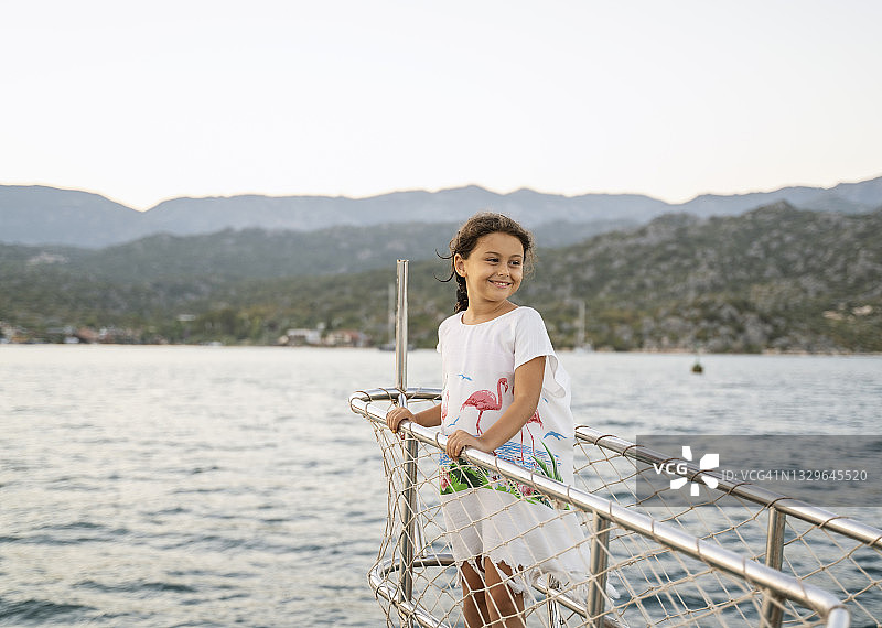 可爱的小女孩在日落时站在帆船的船头图片素材