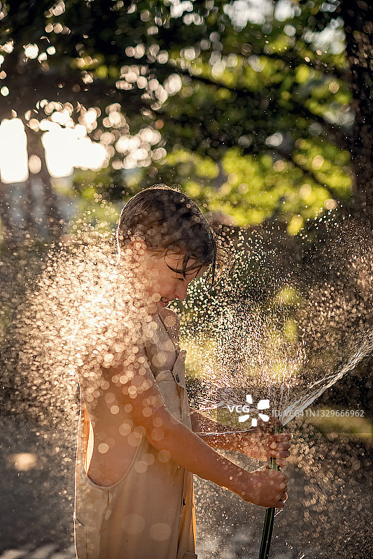 一个男孩在炎热的夏天玩喷水装置。水从软管里飞溅出来。图片素材