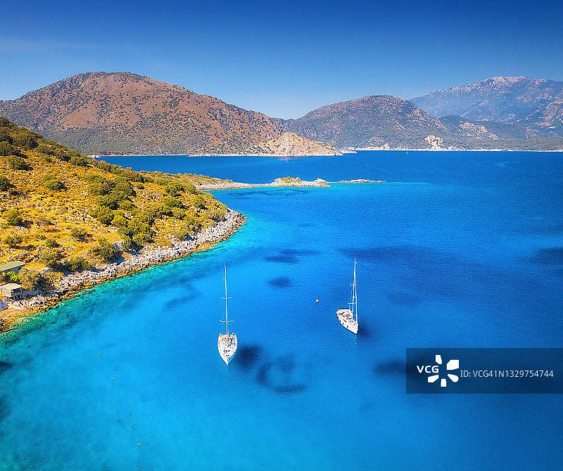 鸟瞰图美丽的游艇和船只在海上在夏季日落在土耳其。豪华游艇，帆船，清澈的蓝色的水，岩石，天空，山和绿色的树木。旅行。景观图片素材