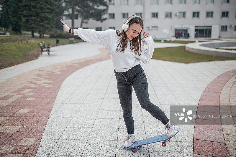微笑的女人在公园里听音乐，玩滑板图片素材