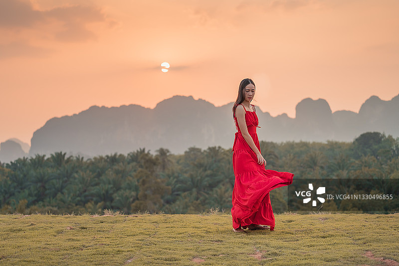 一个穿红衣服的女人在日落时走在山中。图片素材