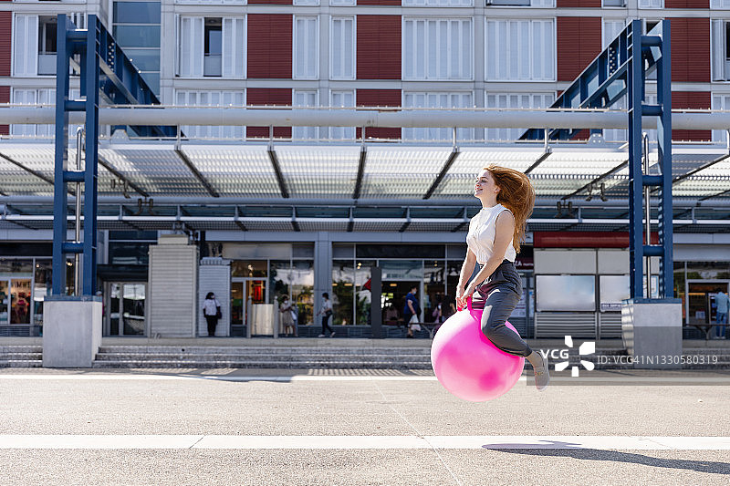 无忧无虑的女性自由职业者与弹跳球通过建筑在阳光灿烂的日子图片素材