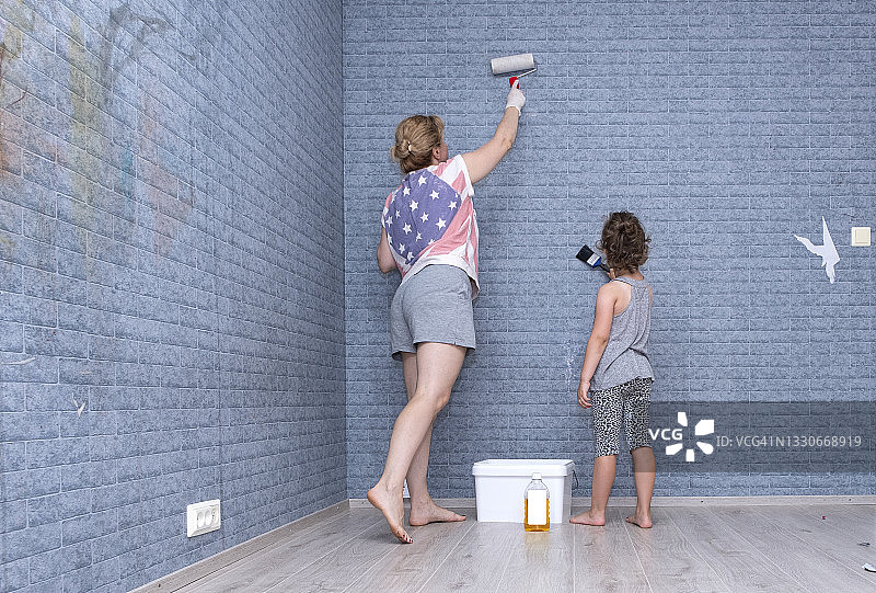 白种人的家庭。一位拿着油漆滚筒的年轻妇女和一个小女孩正在翻修一间儿童房。一个女人在往墙上涂墙纸去除剂。图片素材