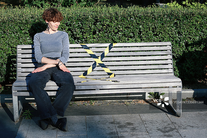年轻的成年妇女交叉双臂和双腿坐在公园的长凳上，用黄色警戒线图片素材