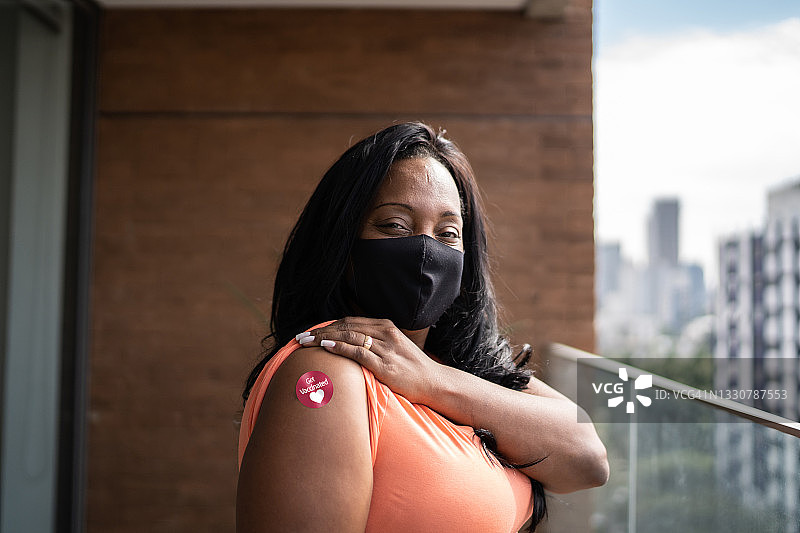 一名戴着防护口罩的成熟女性的肖像，手臂上有“接种过疫苗”的贴纸图片素材