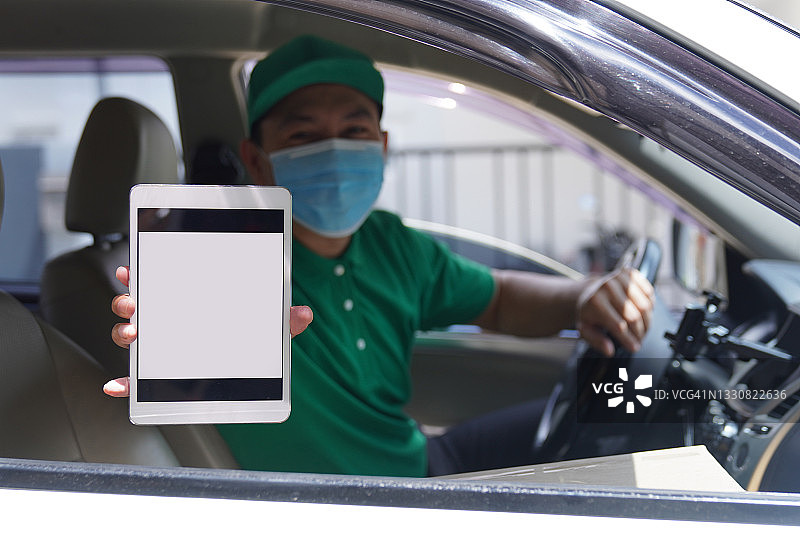 亚洲快递员戴着口罩，身穿绿色制服，在电子平板电脑上显示二维码图片素材