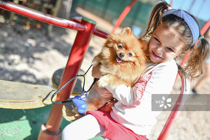 小女孩在操场上拥抱宠物博美犬图片素材