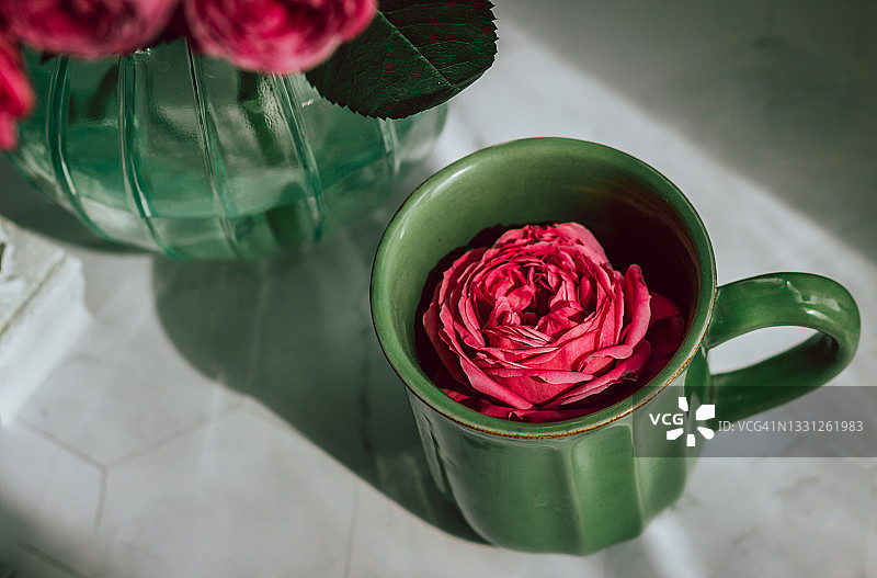 一个绿色的陶瓷杯从上面射出，杯中漂浮着一朵粉红色的玫瑰;旁边是一束玫瑰图片素材