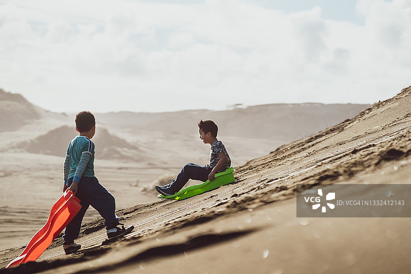孩子们喜欢在户外的沙丘上滑雪。图片素材