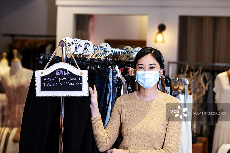 亚洲妇女在服装店靠卖招牌，戴着口罩图片素材