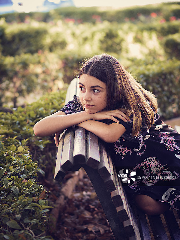 一个十几岁的女孩靠在公园的长椅上。图片素材