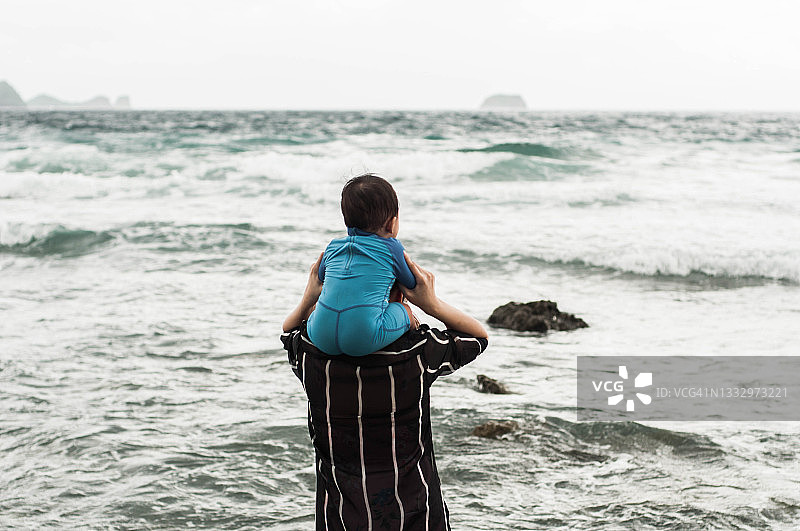 东南亚母亲背着她的儿子，在白天走在海滩上图片素材